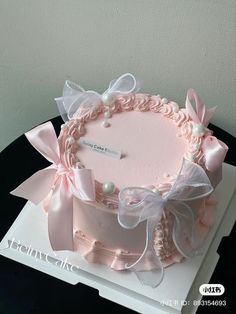 a pink cake decorated with bows and pearls on top of a white table cloth covered box