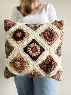 a woman is holding a pillow made with crocheted squares and flowers on it