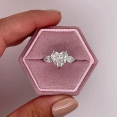 a woman's hand holding an engagement ring in a pink velvet box with three diamonds on it