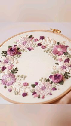 a hand holding a small embroidery kit with pink flowers on the front and purple flowers on the back