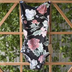 a black and pink floral print swimsuit hanging on a wooden fence with greenery in the background