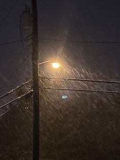 the street light is shining brightly in the dark night, with snow falling all around