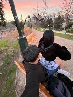 two people sitting on a bench looking out at the sunset or sunrise over a park