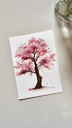 a card with a pink tree on it next to a glass vase and flower pot