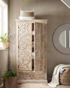 a wooden cabinet sitting in the corner of a room next to a mirror and potted plant