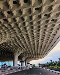 an empty street under a large structure with many holes in it's ceiling and some people walking on the sidewalk