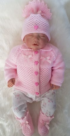 a baby doll wearing a pink knitted outfit and hat on top of a white blanket