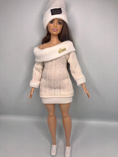 a doll is wearing a white sweater dress and hat with a name tag on it