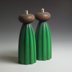 two green vases sitting side by side on a white surface with gold accents and round tops