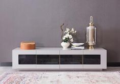 a vase with flowers on top of a white entertainment center table in front of a gray wall