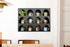 a wall mounted shelf filled with cups on top of a wooden table next to a dining room table