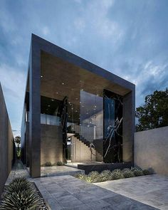 the entrance to a modern house with black and white marble on the outside, surrounded by greenery