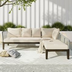 a white couch sitting on top of a cement floor next to a tree and potted plants