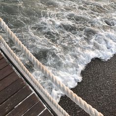 the water is choppy and foamy next to a wooden dock with rope on it