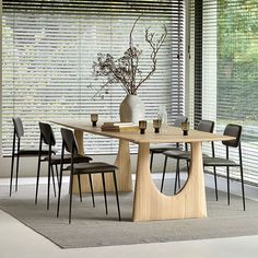 a dining room table with chairs and a vase on the table in front of blinds