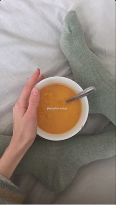 a person holding a bowl of soup on top of a bed with their hands in the bowl