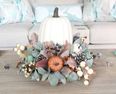 a white pumpkin sitting on top of a wooden table next to flowers and pine cones