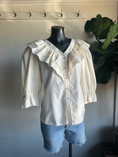 Vintage 1970s Malco Modes Square Dancing Cream Ruffled Blouse. Creamy off white in color made from a cotton/polyester fiber blend. Ruffled accents along shoulders and front of blouse with a button down closure. Lightweight blouse for all day/night comfort. Condition overall is great with no noted flaws. No rips, tears, or staining. Please see all photos for details. Refer to measurements below to ensure a proper fit (modeled on a size medium mannequin) fits a modern L-XL 21" pit to pit 15" shoulder to shoulder (width) 19" sleeves 25" in length (top of shoulder to bottom hem) Square Dance Blouses, White Ruffle Blouse, Square Dancing, 1970s, Womens Clothing Tops, Overalls, Blouses For Women, Fitness Models, Ruffle Blouse