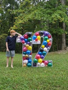 a young boy standing next to the number twenty two made out of balloons and balls