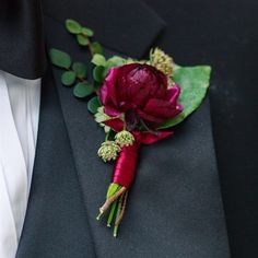 a boutonniere with red flowers and greenery on it's lapel