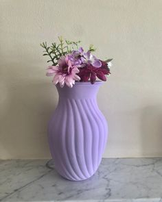 a purple vase with flowers in it sitting on a marble counter top next to a wall