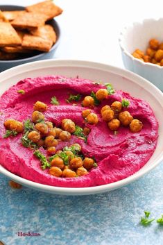 a white bowl filled with red hummus next to crackers