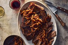 steak with onions on a plate next to two glasses of wine and utensils