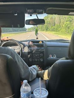 two people sitting in the driver's seat of a car with water bottles on the dash