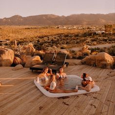 four women sitting in a hot tub on a wooden deck with mountains in the background