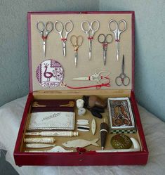 an open red box with scissors and other crafting items in it on a bed