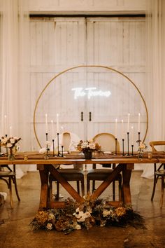 the table is set with candles, flowers and greenery in front of an open door