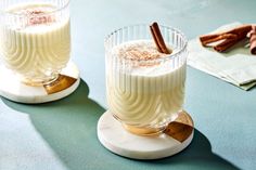 two glasses filled with drink sitting on top of a table next to cinnamon sticks and napkins