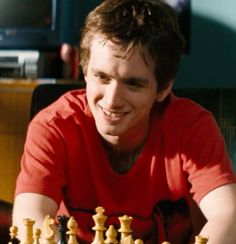 a man sitting at a table next to a chess board with pieces in front of him