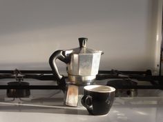 a coffee pot sitting on top of a stove next to a cup filled with liquid