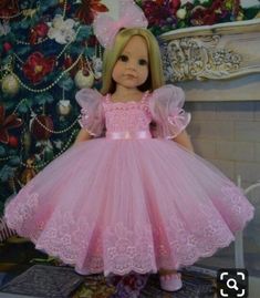 a doll dressed in pink is standing next to a christmas tree