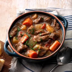 a bowl of beef stew with carrots, potatoes and bread on a wooden table