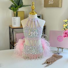 a mannequin is adorned with pink feathers and beads on a white table in front of flowers