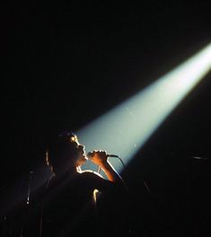 a man standing in front of a microphone on top of a stage with bright light coming from behind him