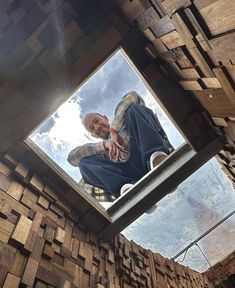 a man sitting on top of a wooden structure next to a skylight with clouds in the background