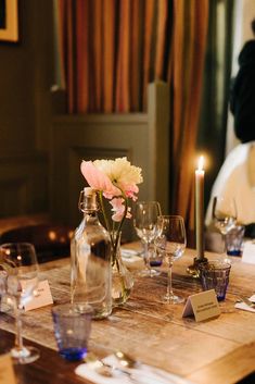 a wooden table topped with wine glasses and a vase filled with flowers next to a candle