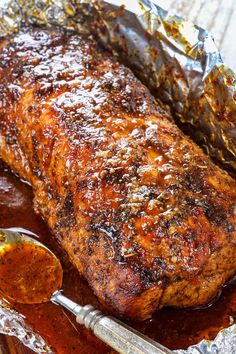 a piece of meat covered in sauce with a spoon next to it on tin foil