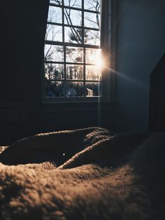 the sun shines brightly through an open window on a bed in a dark room