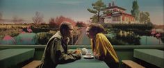 two men are sitting at a table talking to each other in front of a painting