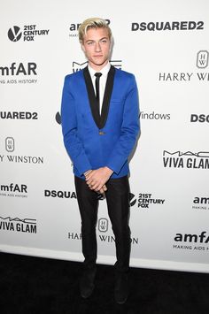 a man in a blue suit and black tie standing on a red carpet at an event