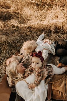 two women and a baby laying on a blanket in the middle of some dry grass