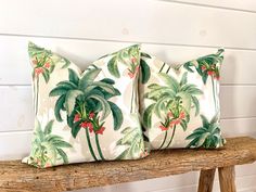 three pillows with palm trees on them sitting on a wooden bench in front of a white wall