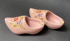 two pink ceramic shoes with flowers painted on them sitting on a gray surface, next to each other