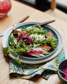 there is a salad on the table with two bowls and utensils next to it