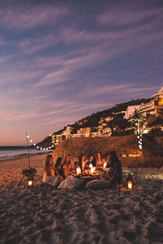 a group of people sitting on top of a sandy beach next to the ocean at night