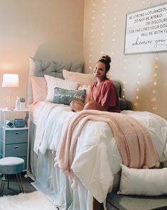 a woman sitting on top of a bed next to a night stand with lights hanging above it